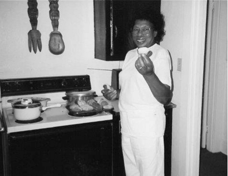 A woman standing next to a stove holding up a bread roll.